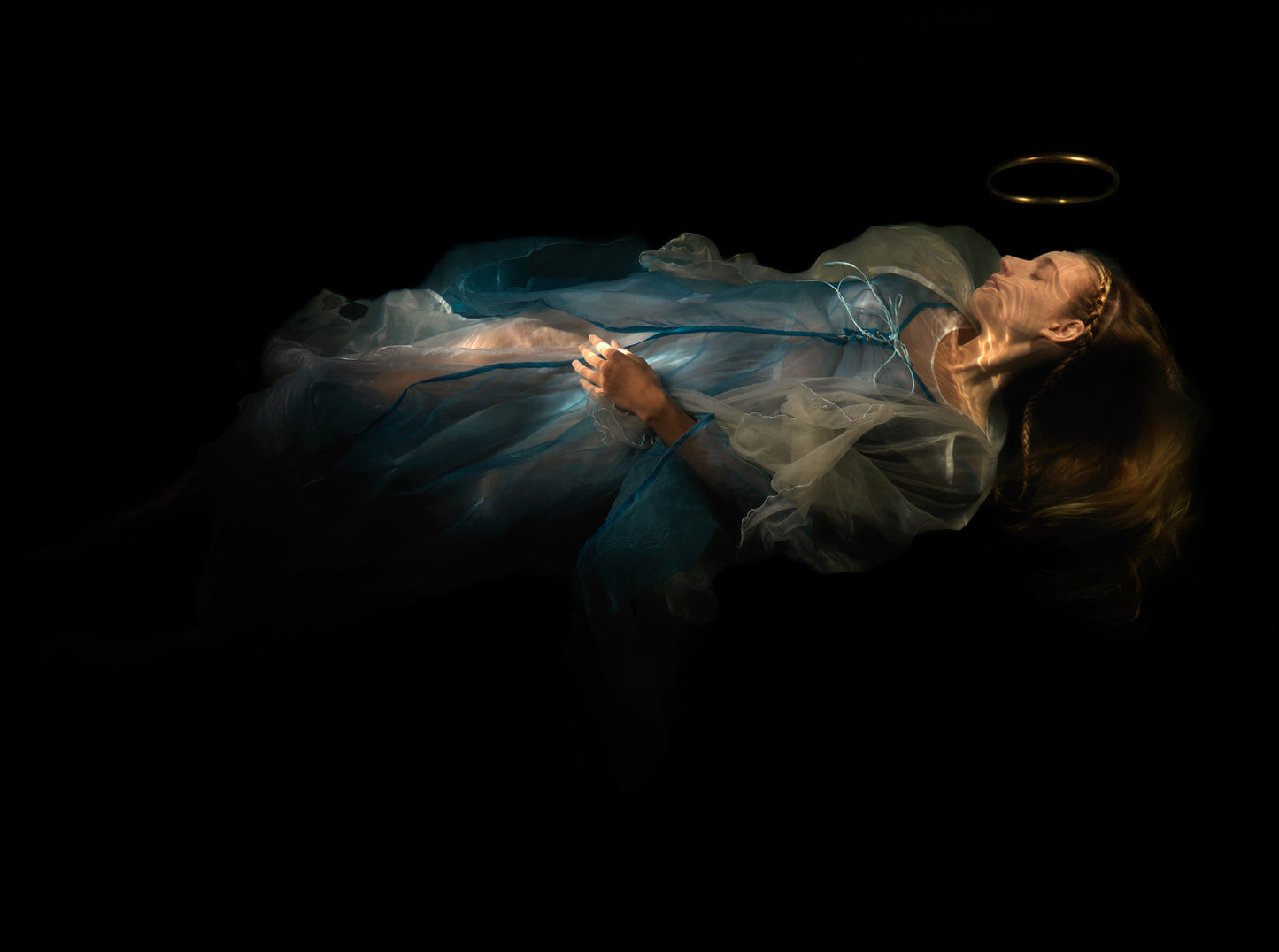 Unique archival pigment print of a woman lying down in flowing blue and white fabric on black background.