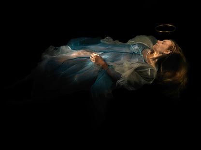 Unique archival pigment print of a woman lying down in flowing blue and white fabric on black background.